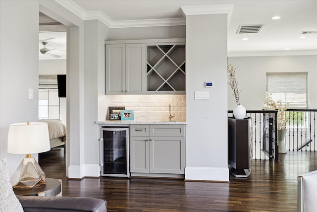 indoor dry bar featuring wine cooler, dark wood-type flooring, decorative backsplash, healthy amount of natural light, and ornamental molding