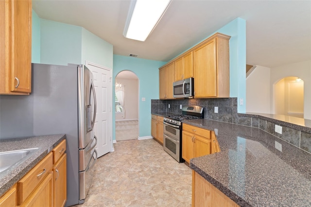 21514 Skyla Cir, Humble, TX 77338 - kitchen featuring appliances with stainless steel finishes, arched walkways, tasteful backsplash, and dark stone countertops