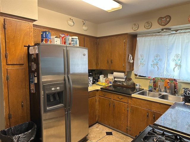 kitchen with stainless steel refrigerator with ice dispenser, brown cabinetry, a sink, and light tile patterned floors
