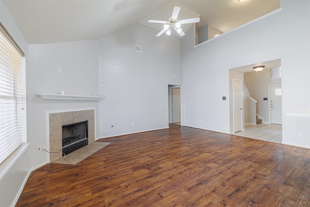 unfurnished living room with a ceiling fan, wood finished floors, a fireplace, high vaulted ceiling, and stairs