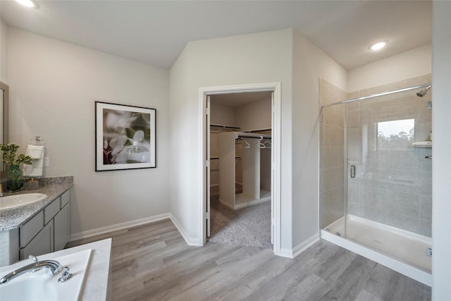 full bath with a stall shower, wood finished floors, a spacious closet, vanity, and recessed lighting