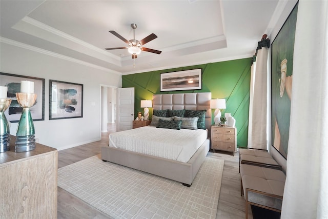 bedroom with a tray ceiling, ornamental molding, light wood finished floors, baseboards, and a ceiling fan