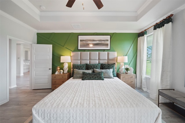 bedroom with a tray ceiling, wood finished floors, crown molding, and ceiling fan
