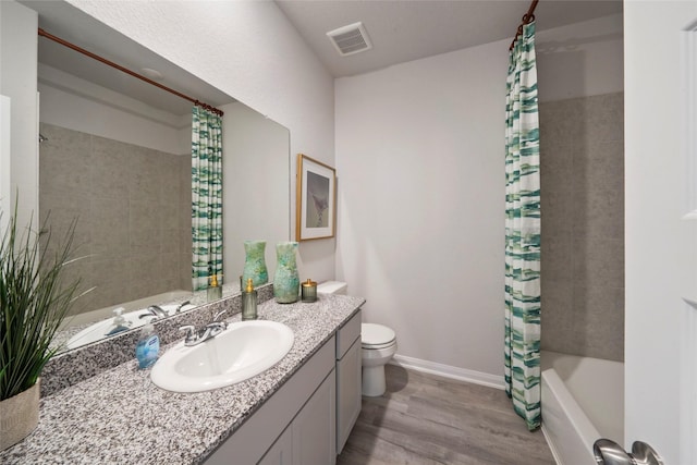 bathroom with wood finished floors, toilet, vanity, shower / tub combo, and baseboards