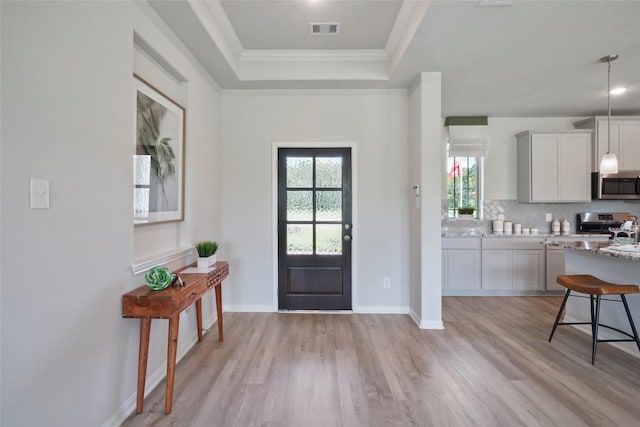 foyer featuring light wood finished floors, a tray ceiling, crown molding, and baseboards