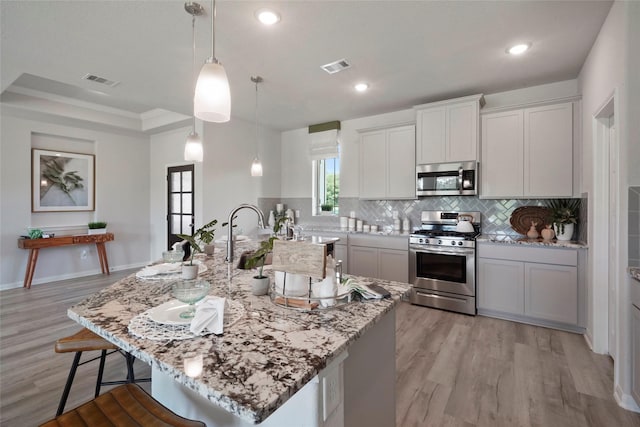 kitchen with appliances with stainless steel finishes, backsplash, a kitchen bar, light wood-style flooring, and recessed lighting