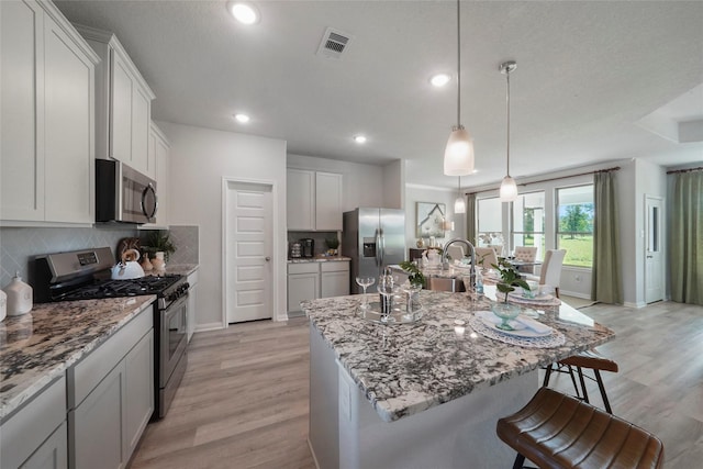 kitchen featuring stainless steel appliances, light wood finished floors, a kitchen bar, decorative backsplash, and recessed lighting
