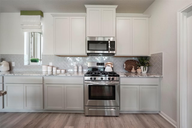 kitchen featuring appliances with stainless steel finishes, light wood-style flooring, tasteful backsplash, and light stone counters