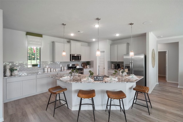kitchen with stainless steel appliances, a large island with sink, backsplash, light wood-type flooring, and recessed lighting