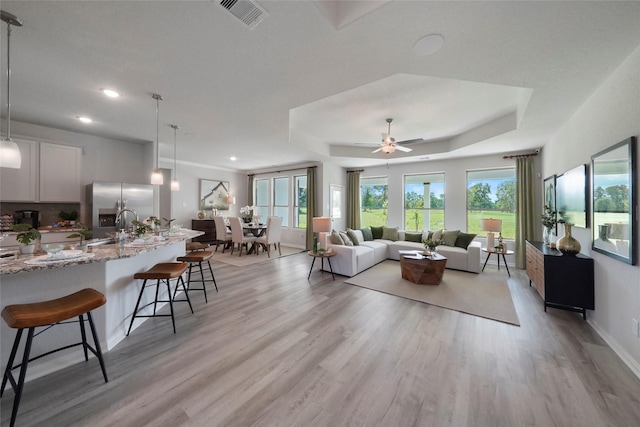 living area with light wood-style floors, a ceiling fan, a raised ceiling, baseboards, and recessed lighting