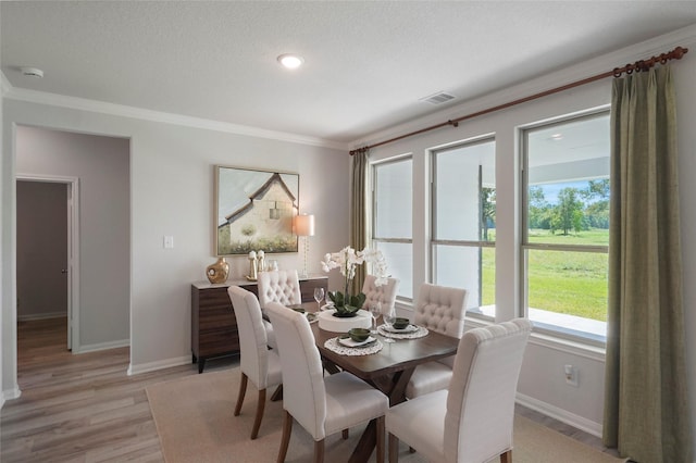 dining area featuring ornamental molding, light wood-type flooring, baseboards, and a textured ceiling