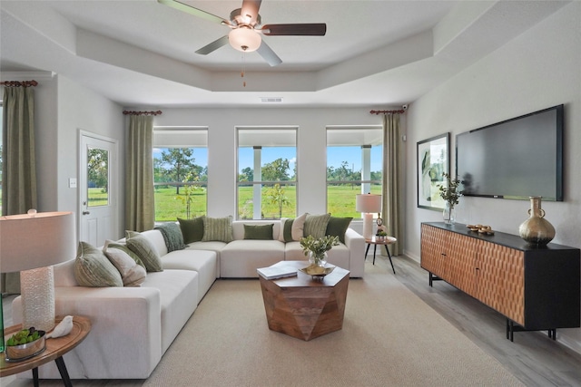 living area featuring plenty of natural light, a ceiling fan, wood finished floors, and a tray ceiling