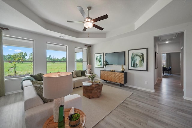 living room featuring a raised ceiling, attic access, light wood-style flooring, and healthy amount of natural light