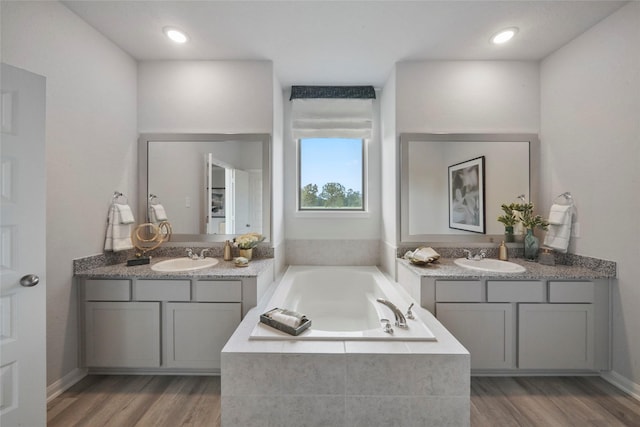 full bath featuring two vanities, a bath, and wood finished floors