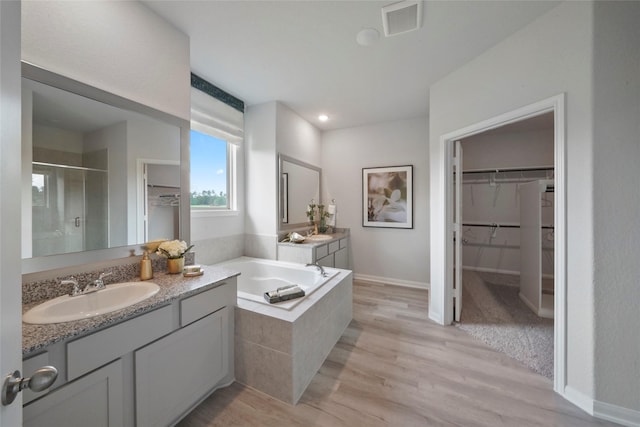 full bathroom with a shower stall, a spacious closet, wood finished floors, a garden tub, and vanity