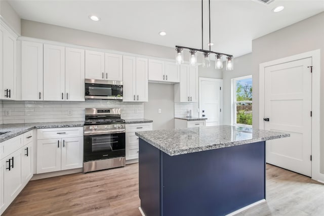 kitchen featuring stainless steel appliances, white cabinetry, light stone countertops, decorative backsplash, and light wood-type flooring