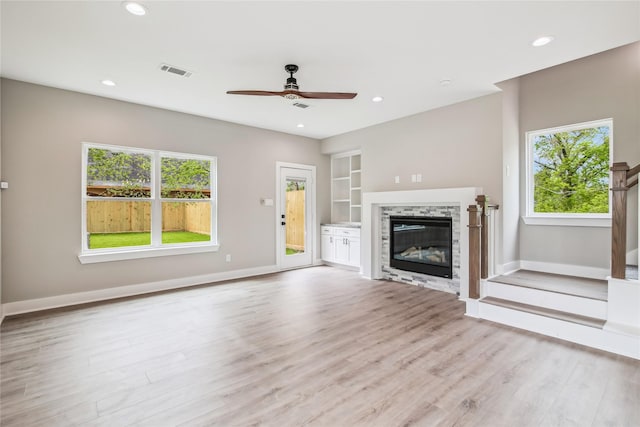 unfurnished living room featuring a ceiling fan, wood finished floors, baseboards, a glass covered fireplace, and built in shelves