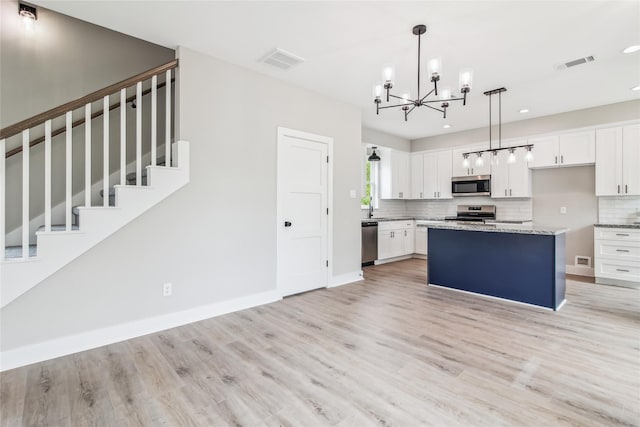 kitchen with appliances with stainless steel finishes, a chandelier, light wood-style floors, decorative backsplash, and white cabinets