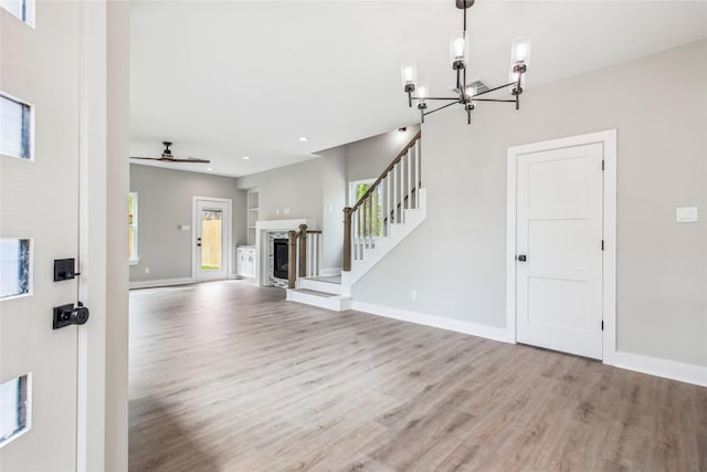 unfurnished living room with light wood-type flooring, a chandelier, stairs, baseboards, and recessed lighting
