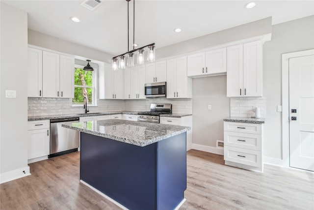 kitchen with appliances with stainless steel finishes, a sink, light stone countertops, backsplash, and white cabinets