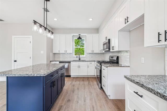 kitchen featuring appliances with stainless steel finishes, blue cabinetry, a sink, light wood-style flooring, and backsplash