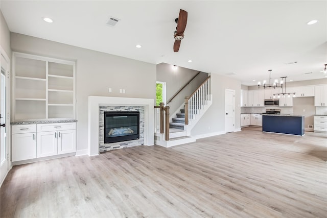 unfurnished living room featuring a glass covered fireplace, light wood-style flooring, stairs, a chandelier, and recessed lighting