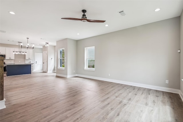 unfurnished living room featuring a ceiling fan, baseboards, light wood-style floors, recessed lighting, and a chandelier