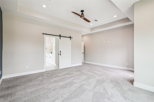 unfurnished bedroom with a barn door, a raised ceiling, carpet, baseboards, and recessed lighting