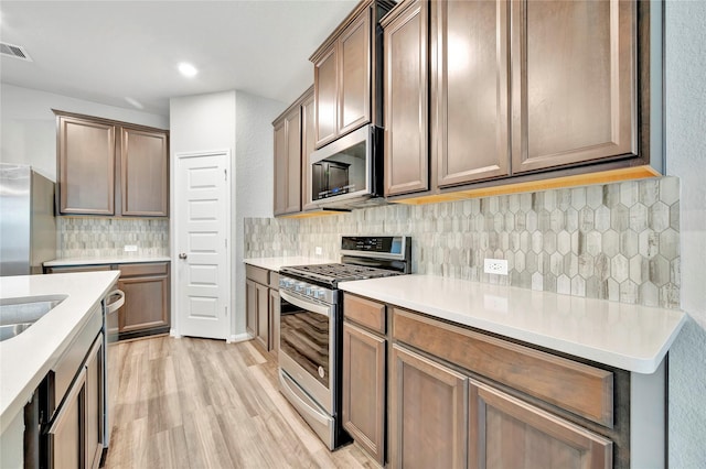 kitchen featuring stainless steel appliances, light wood finished floors, tasteful backsplash, light countertops, and recessed lighting