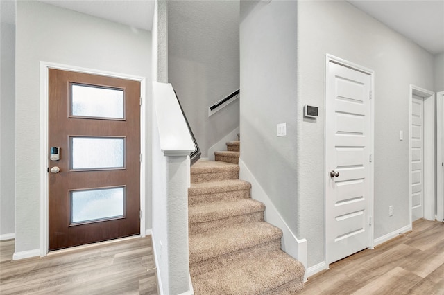 foyer featuring light wood finished floors, stairs, plenty of natural light, and baseboards