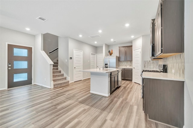 kitchen featuring stainless steel fridge with ice dispenser, light wood finished floors, tasteful backsplash, light countertops, and a kitchen island with sink