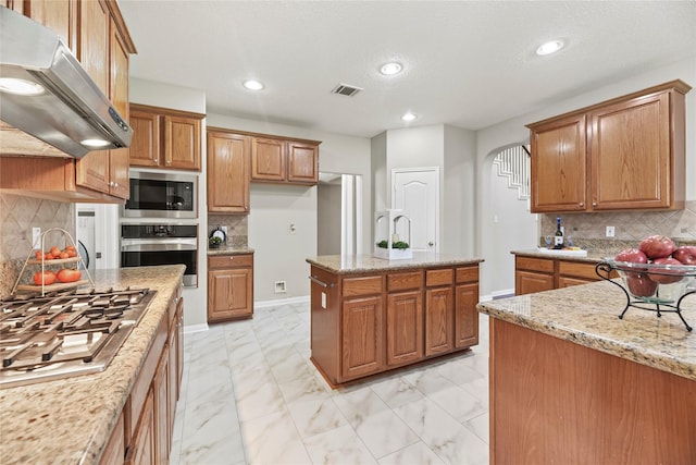 17406 Lonesome Dove Trl, Houston, TX 77095 - kitchen with stainless steel appliances, under cabinet range hood, light marble finish flooring, brown cabinetry, and recessed lighting