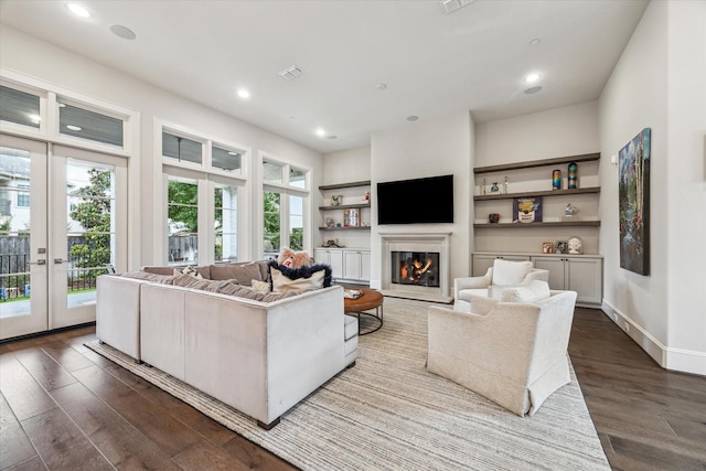 living area with dark wood-style flooring, a glass covered fireplace, recessed lighting, baseboards, and built in features