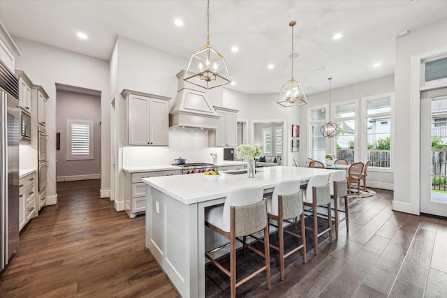 kitchen featuring recessed lighting, light countertops, a breakfast bar, a kitchen island with sink, and dark wood finished floors