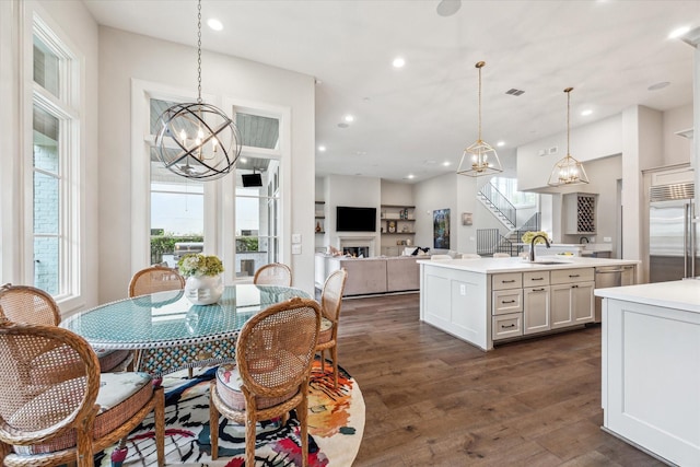 dining room featuring dark wood finished floors, a chandelier, stairs, a warm lit fireplace, and recessed lighting