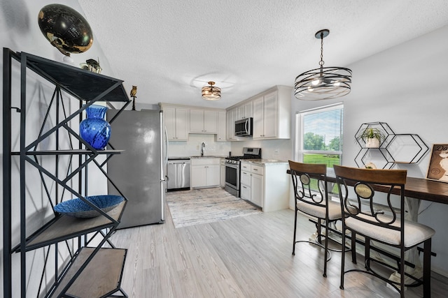 5024 County Road 476a, Freeport, TX 77541 - kitchen featuring appliances with stainless steel finishes, light wood finished floors, a textured ceiling, hanging light fixtures, and white cabinets