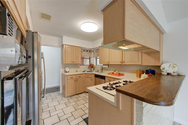 kitchen featuring light brown cabinetry, a peninsula, stainless steel dishwasher, and a sink