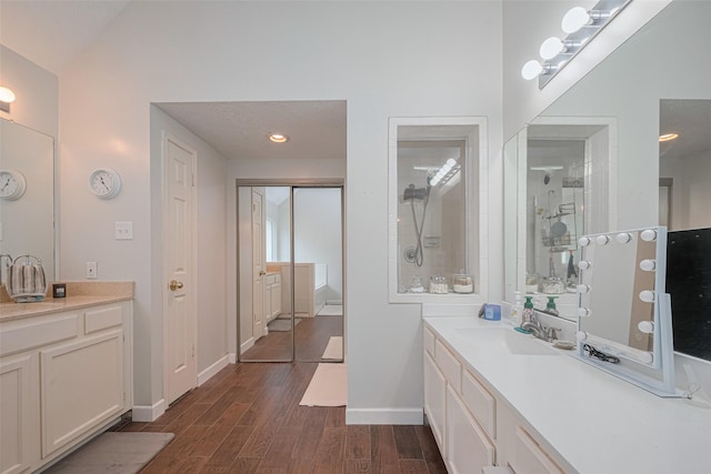 bathroom featuring wood finished floors, baseboards, a tile shower, and vanity