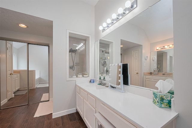 bathroom featuring a tile shower, wood finished floors, baseboards, and vanity