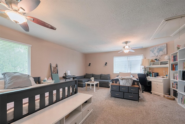 bedroom with attic access, a textured ceiling, carpet, an office area, and a ceiling fan
