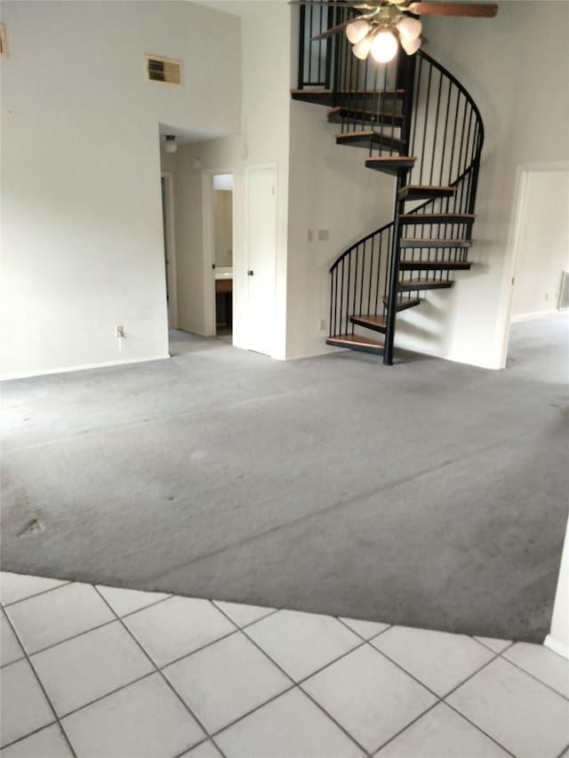 unfurnished living room with carpet flooring, a high ceiling, a ceiling fan, and stairway