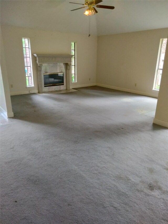 unfurnished living room featuring a ceiling fan, carpet floors, baseboards, vaulted ceiling, and a premium fireplace