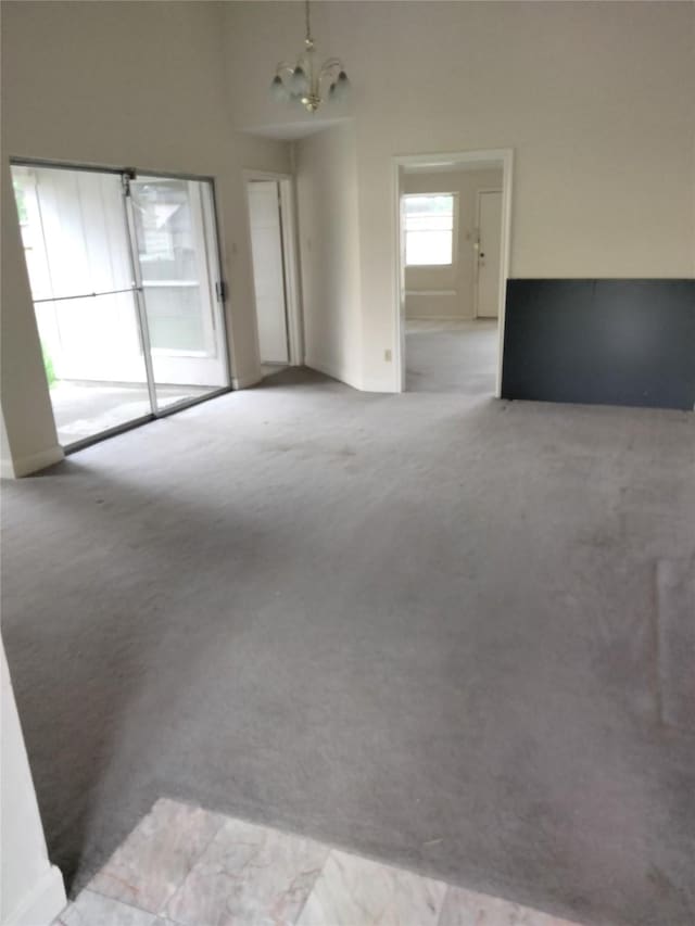 empty room with a chandelier, light carpet, and baseboards