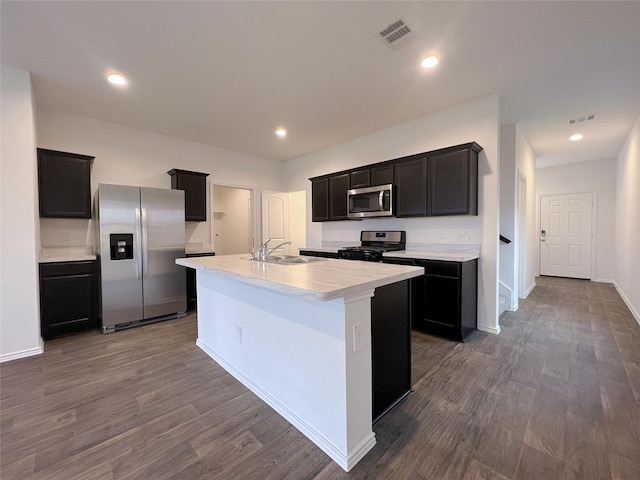 21310 Black Leaf Dr, New Caney, TX 77357 - kitchen featuring appliances with stainless steel finishes, light countertops, dark cabinetry, an island with sink, and dark wood finished floors