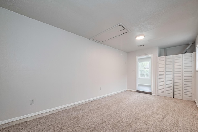 spare room featuring attic access, carpet flooring, and baseboards