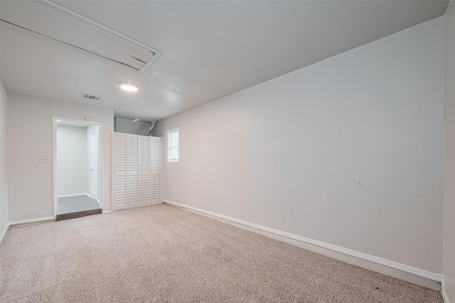 carpeted spare room with attic access and baseboards