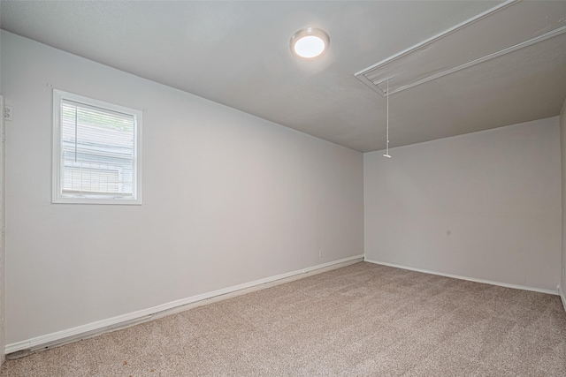 carpeted empty room featuring attic access and baseboards