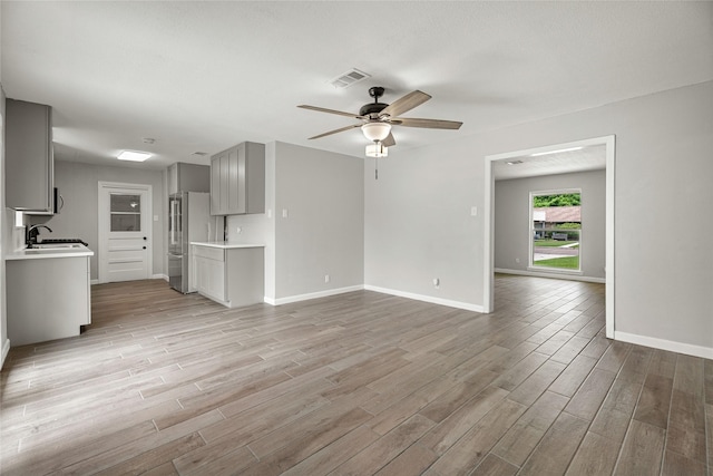 unfurnished living room with light wood-style floors, ceiling fan, baseboards, and a sink
