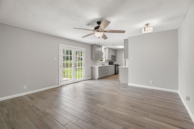 unfurnished living room featuring a sink, ceiling fan, light wood-type flooring, baseboards, and a textured ceiling