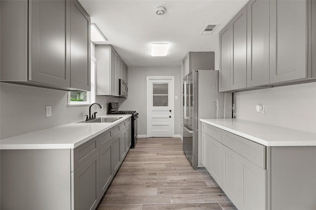kitchen with appliances with stainless steel finishes, gray cabinetry, a sink, and light countertops